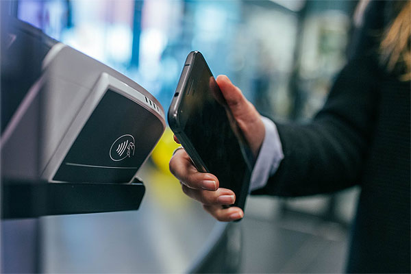 Frau hält ein Smartphone an ein NFC Terminal