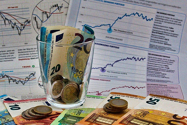 Euro-Banknoten und Münzen, im Hintergrund Kursdiagramme